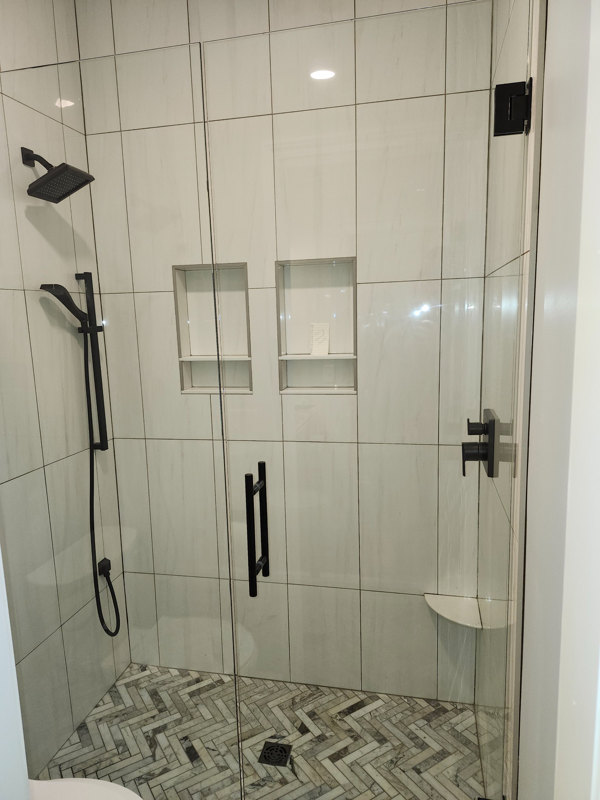 Glass-enclosed tile shower with matte black fixtures and herringbone floor